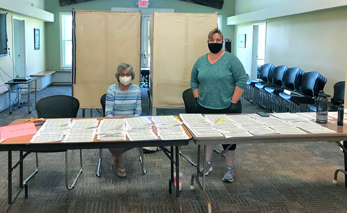 A masked volunteer and Assistant Town Clerk/Treasurer Christina Booher, along with Town Clerk/Treasurer Mary Mead, checked in voters and accepted ballots at a table at the entrance of Town Hall on Tuesday. Photo by Chea Waters Evans