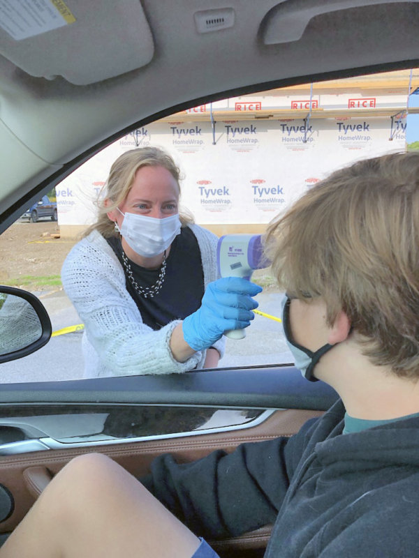 Charlotte Central School Co-principal Jen Roth takes a student’s temperature in the drop-off line in the school parking lot last week. All students get temperature checks before they enter the building. Roth gives them the go-ahead with a cheerful, “You’re healthy!” Photo by Chea Waters Evans