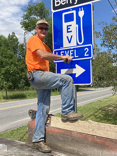 Jr Lewis on Ferry Road installing the sign that the CEC got from VTrans to point the way to the electric vehicle charger at Town Hall. VTrans also installed signage on Route 7, so now there’s no missing it! Photo by Rebecca Foster