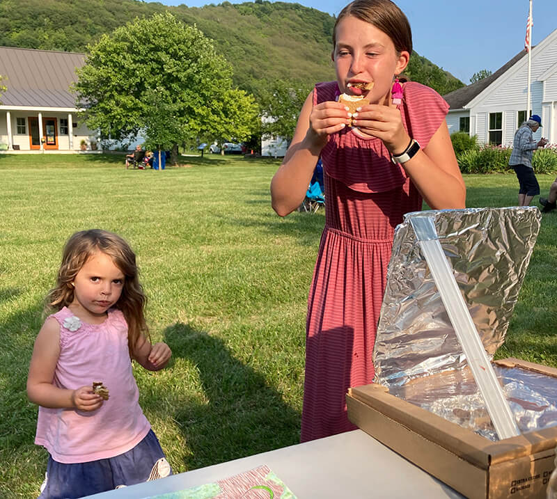Cousins Brynn Herlihy and Chapin Grubbs dig in after learning how the solar oven works. At the next concert on Aug.12, they’ll get to learn how to work the smoothie bike that the Charlotte Energy Committee is borrowing from City Market.Photos by Rebecca Foster 