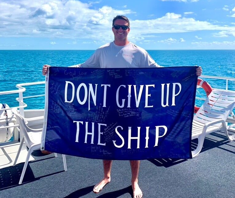 Courtesy photo Kyle Jaunich on a dive trip to the Bahamas. The ‘don’t give up the ship’ banner was signed by all of his doctors and nurses every time he went into a hospital. While at the Naval Academy, he did a semester at sea, so there are also pictures of him and the banner at places like the Great Wall of China and on Table Mountain in South Africa.