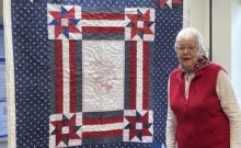 Photo by Lori York. Ruth Whitaker of Shelburne stands with a quilt created by members of Quilts of Valor, whose mission is to cover service members and veterans touched by war with quilts.