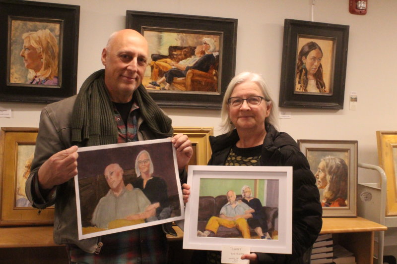 Photo by Scooter MacMillan. Tom Marrinson and Allison Beach hold two different versions of themselves and a third hangs behind and between them on the wall at the Charlotte Library art exhibit.