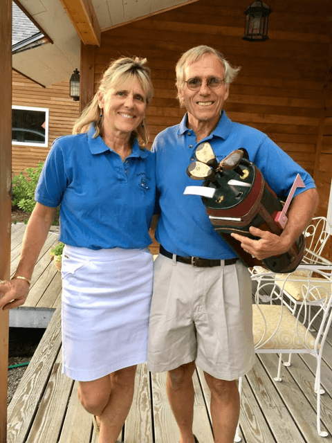 Courtesy photoEbeth and Tom Scatchard on the deck of their homemade home. Tom is holding a mail box designed to look like golf clubs for one of the Memorial Day tournaments they hold on their homemade golf course.