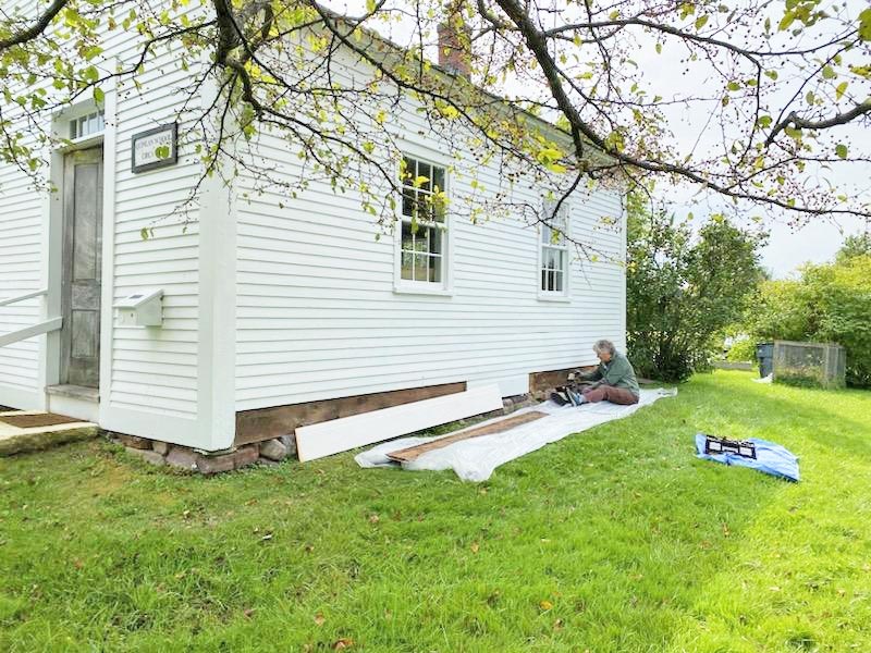 Photo by Janet Yantachka.  Jenny Cole works on the siding of the Quinlan Schoolhouse next to the library. She has done a lot of restoration work on the building this past summer.