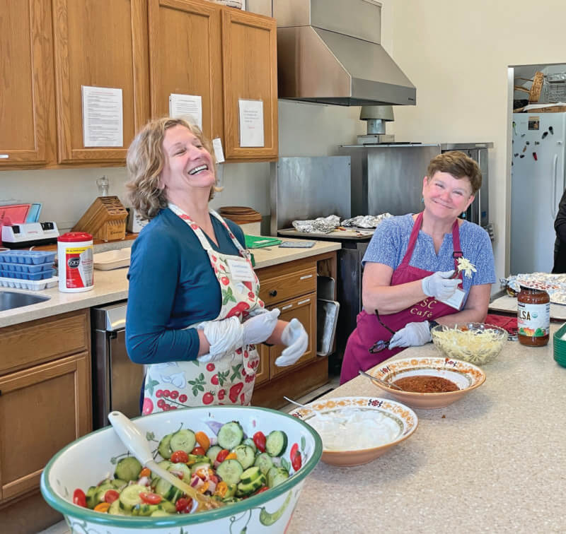 Photo by Lori York. Volunteers Carol Geske (left) and Sue Foley share some laughter as they prep for the Monday lunch.