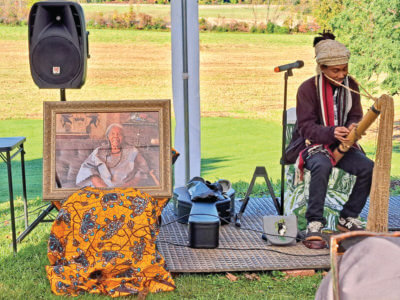 Photo by Mike Yantachka A picture of Lydia Clemmons Sr. sits in honor at a celebration of her legacy at the Clemmons Family Farm while musician Mikahely plays a valiha, a stringed instrument from Madagascar made from bamboo.