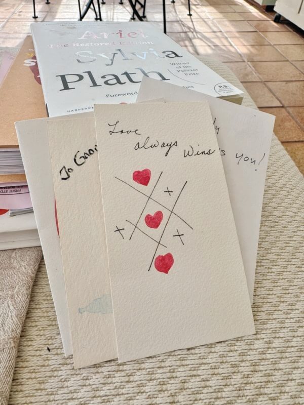 A table in Joan Weed’s garden room is filled with poetry, cooking and gardening books she’s reading and samples of the Valentines she’s been painting for her grandchildren for 33 years.