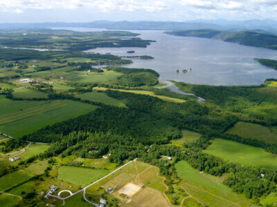 An aerial view of Williams Woods Natural Area and conserved farmland with Lake Champlain in the distance.