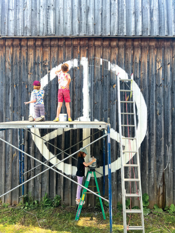 Three volunteers paint a peace sign on the Farmer Barn in Burlington’s Intervale.