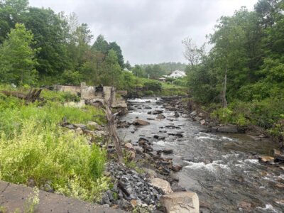 Photo by Elise Coyle. In the summer of 2025, the remains of the old dam cling to the banks of the Winooski River in Cabot
