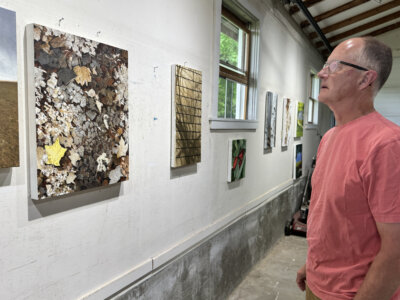 Photo by Scooter MacMillan. Peter Joslin contemplates some of his paintings in his studio on One Mile Road in East Charlotte